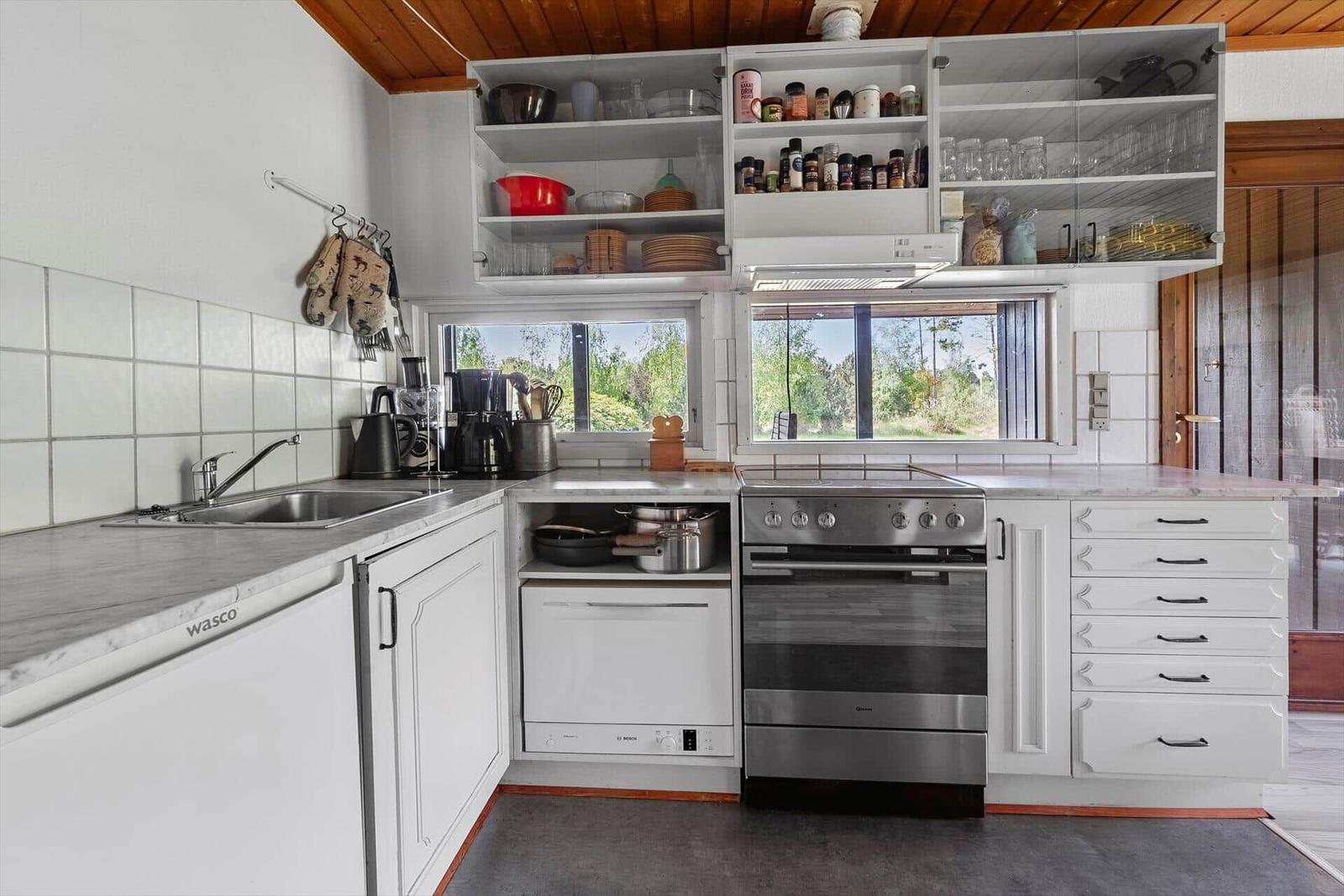 Küche mit weißen Schränken, Edelstahlherd und Fenstern zum Garten.