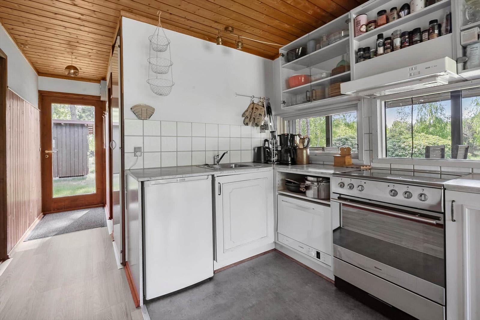 Küche mit weißen Schränken, Edelstahlspüle und Fenster zur Außenseite.