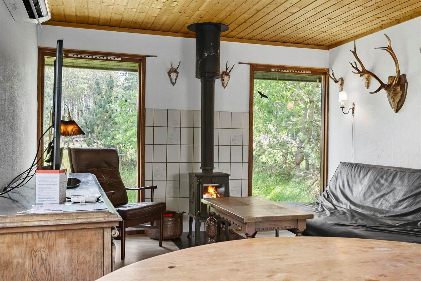 Wohnraum mit Kamin, Sofa und Blick auf Wald.