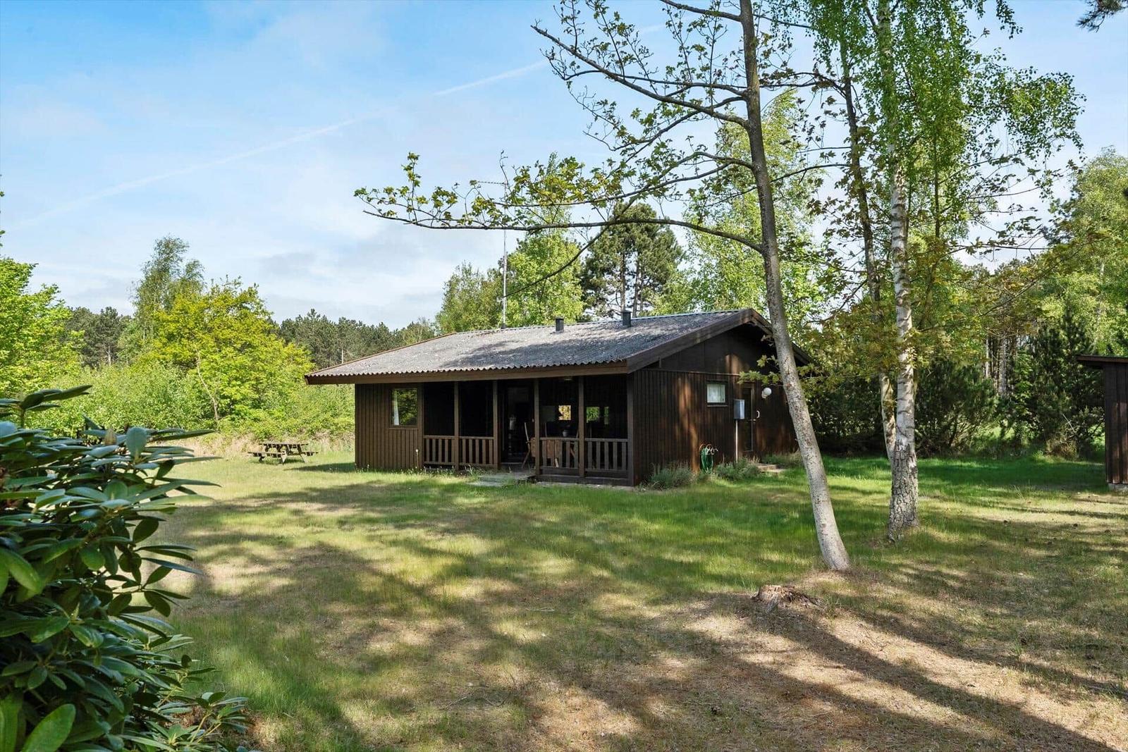 Holzhütte mit Terrasse im Grünen, umgeben von Bäumen und Gras.