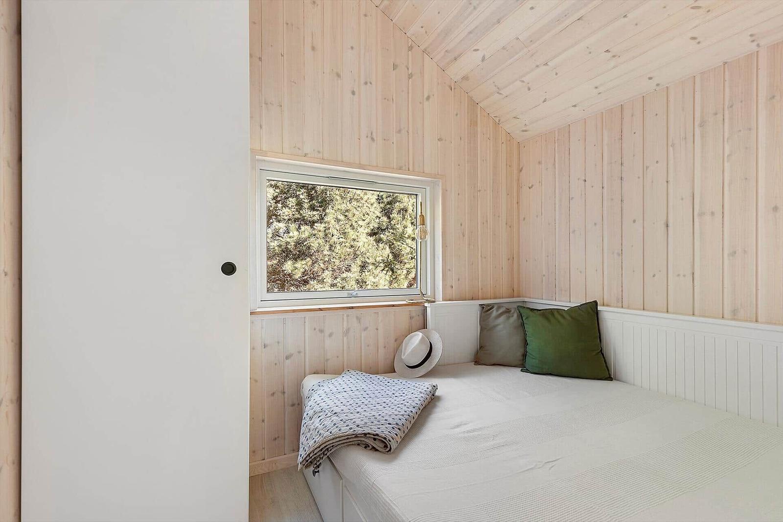 Schlafzimmer mit Holzwand und Fensterblick auf Bäume