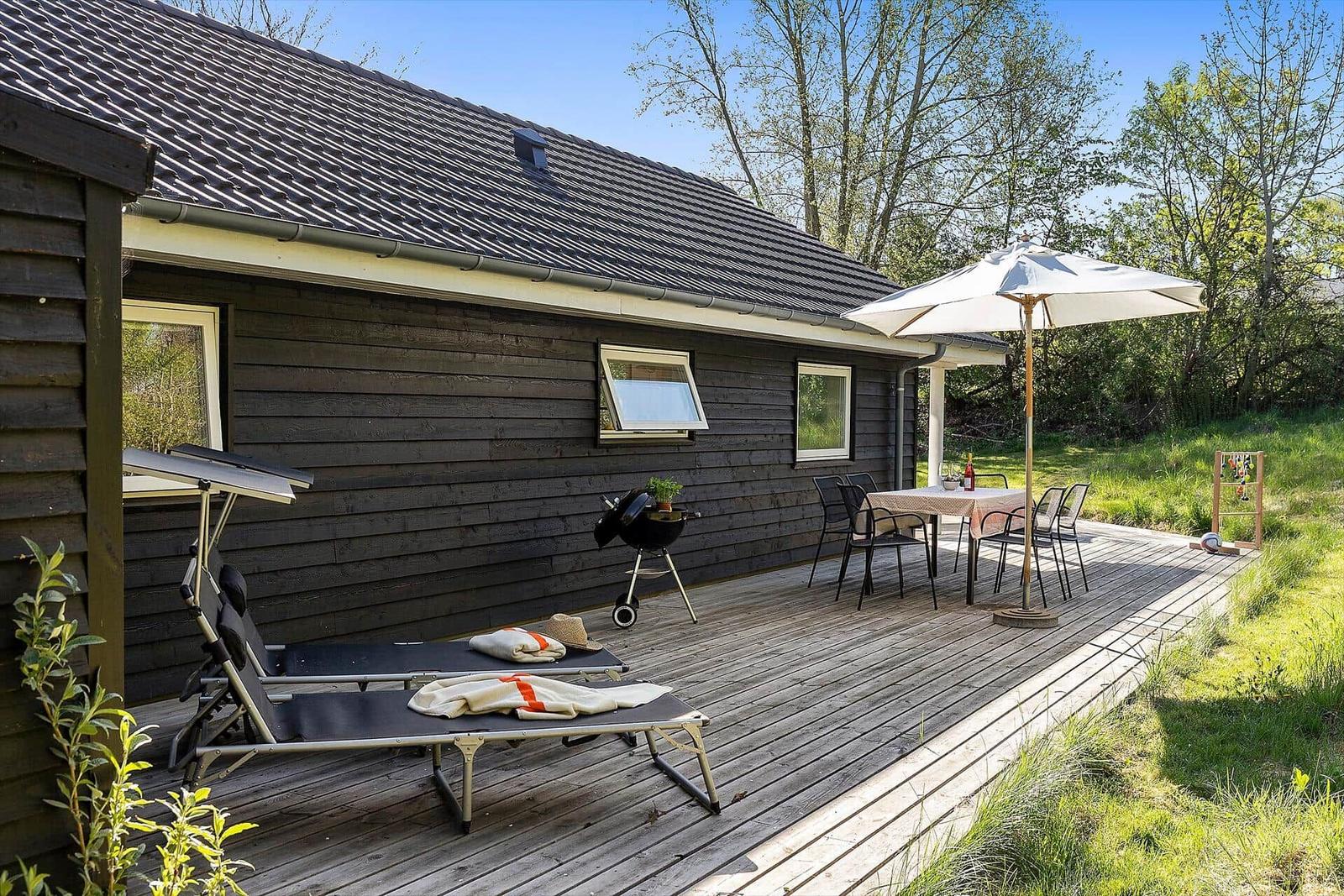 Holzterrasse mit Sonnenliegen, Grill und Tisch mit Sonnenschirm.