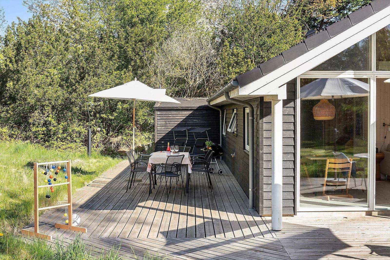 Terrasse mit Tisch, Stühlen und Sonnenschirm. Holzterrasse, umgeben von Grün.