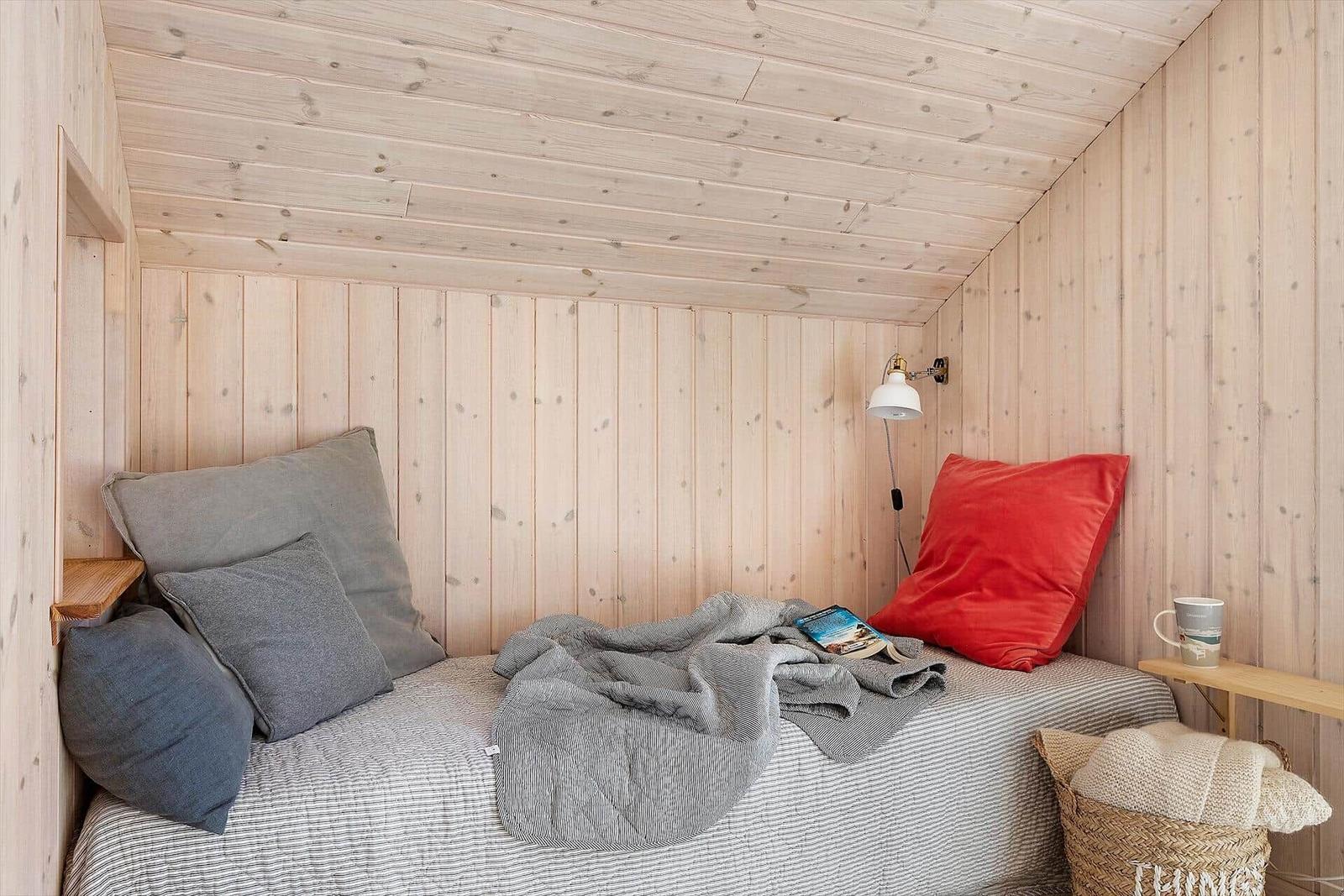 Ein Bett mit Kissen und Decke in einem Holzraum mit Wandlampe.