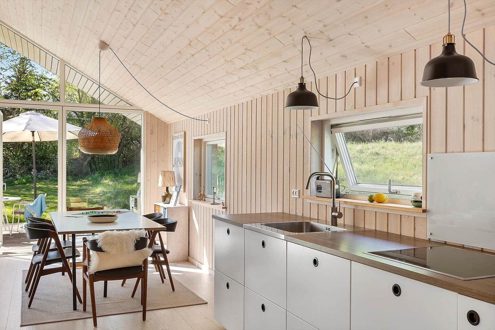 Küche und Essbereich mit Holzwand, Tisch, Stühlen und Fenster zur Außenterrasse.