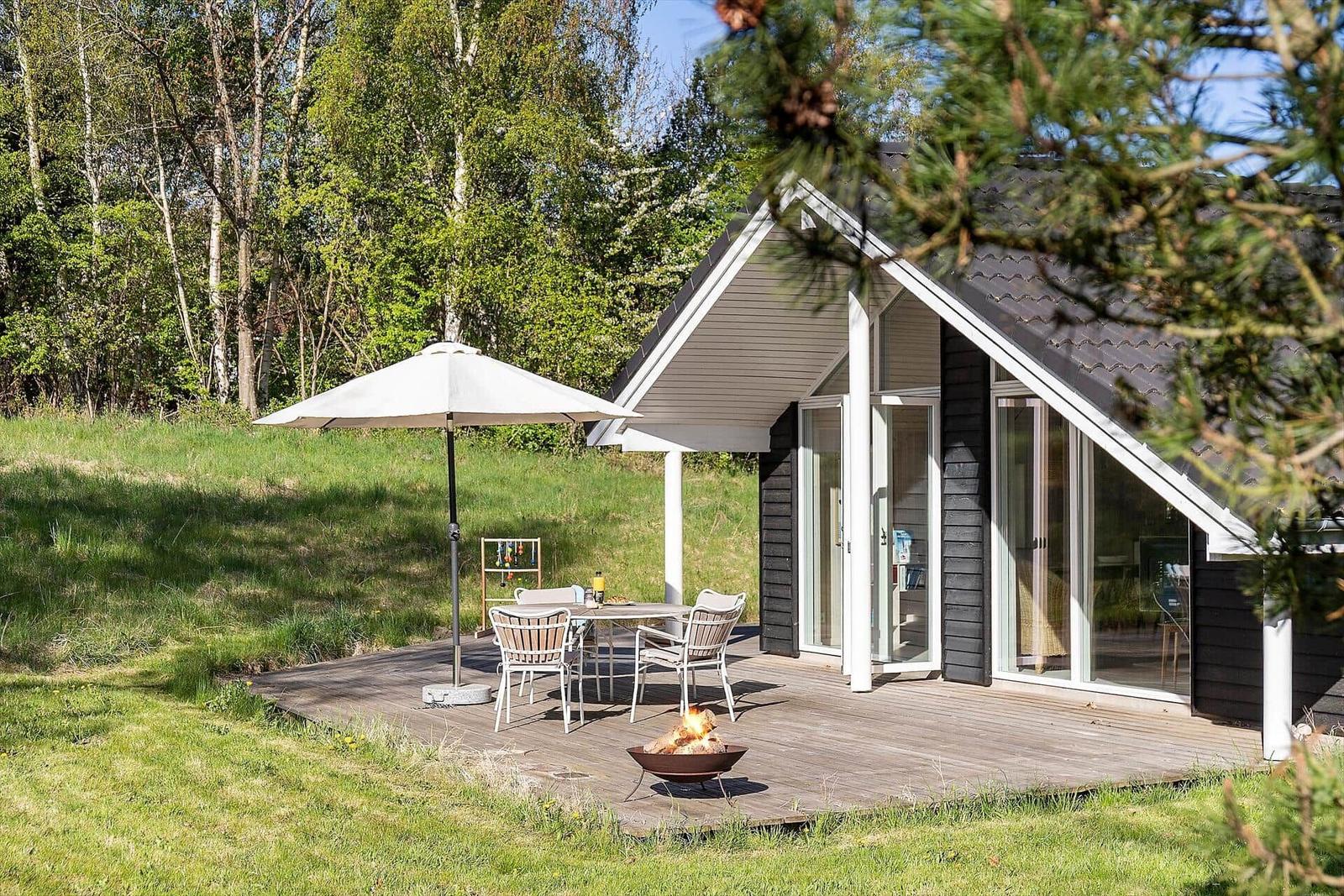 Haus mit Terrasse, Tisch, Stühlen, Sonnenschirm und Feuerkorb.