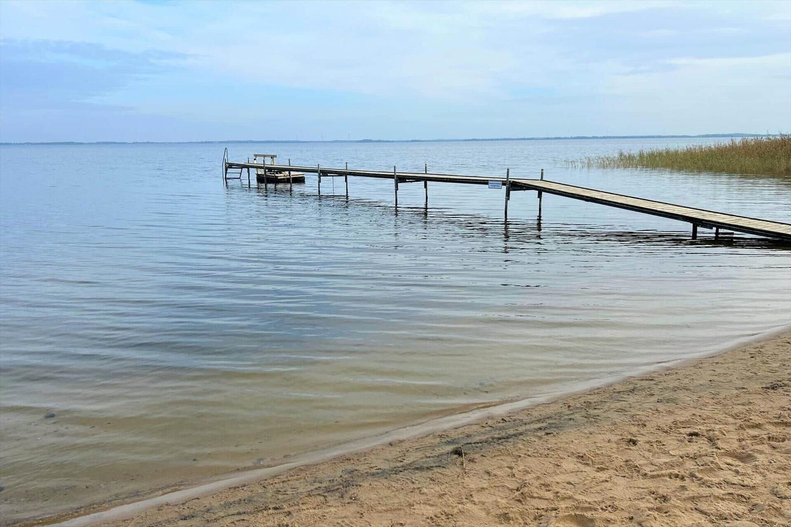 Wooden pier extends into the water. Sandy beach and calm water.