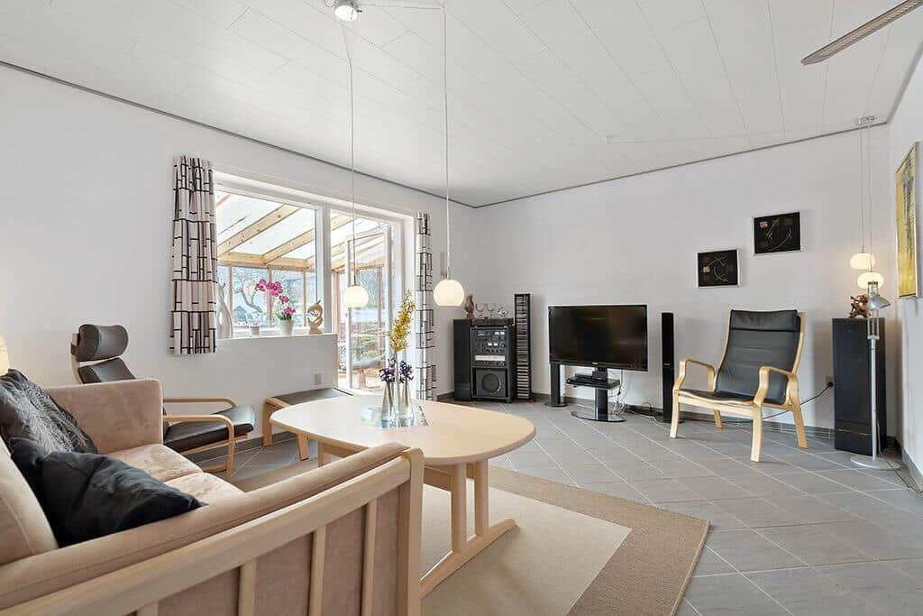 Wohnzimmer mit Sofa, Couchtisch, Fernseher und Sessel. Fenster mit Blick auf Terrasse.