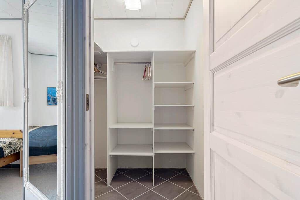 Ein Kleiderschrank mit Regalen und Stange. Durchgehendes Spiegelglas an der Tür.