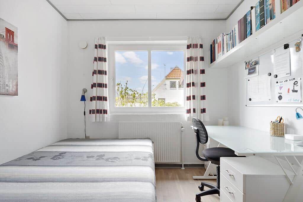 Schlafzimmer mit Schreibtisch, Fenster und Bücherregal an der Wand.