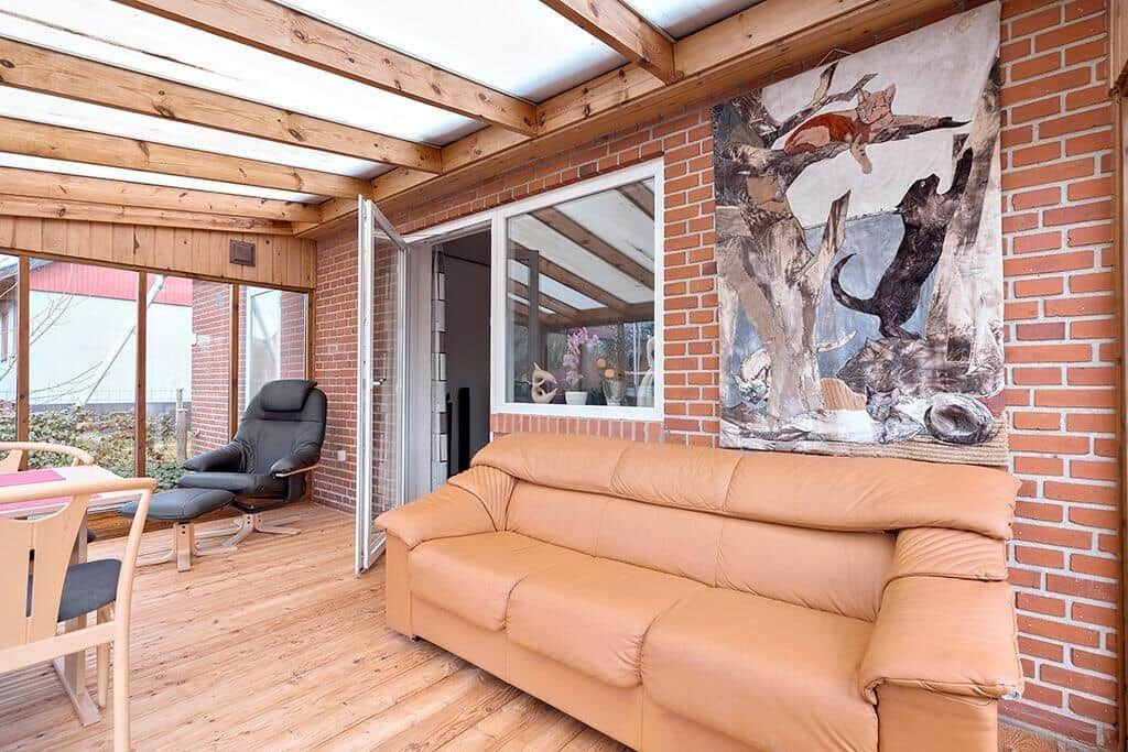 Wohnbereich mit Sofa, Sessel und Wandbild an Backsteinwand.