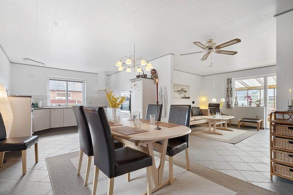 Essbereich mit Tisch und Stühlen, Küche und Wohnbereich mit Sofa und Fenster.