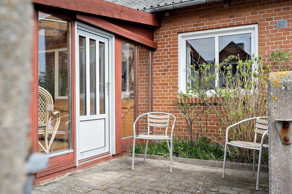 Haus mit Terrasse, weiße Tür, zwei Stühle und Pflanzen.