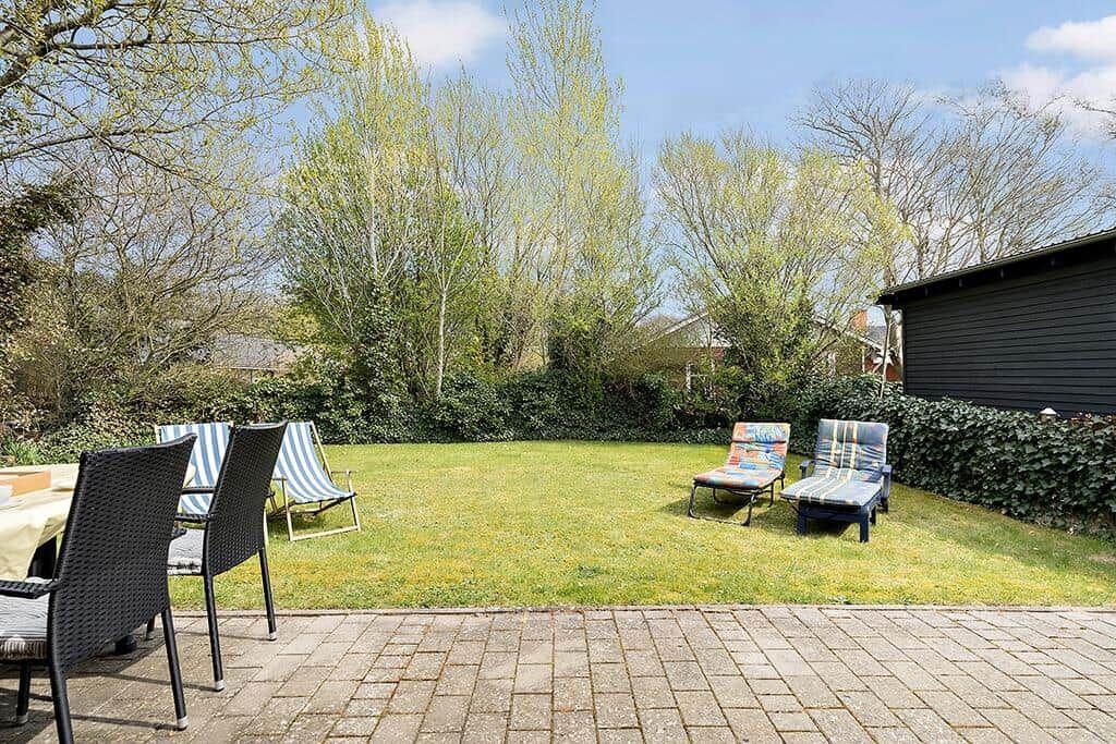 Hinterhof mit Rasenfläche, Sonnenliegen und Tisch mit Stühlen.