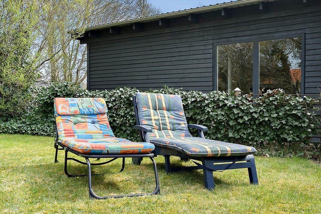 Zwei Liegestühle mit bunten Kissen stehen auf dem Rasen vor einem Haus.