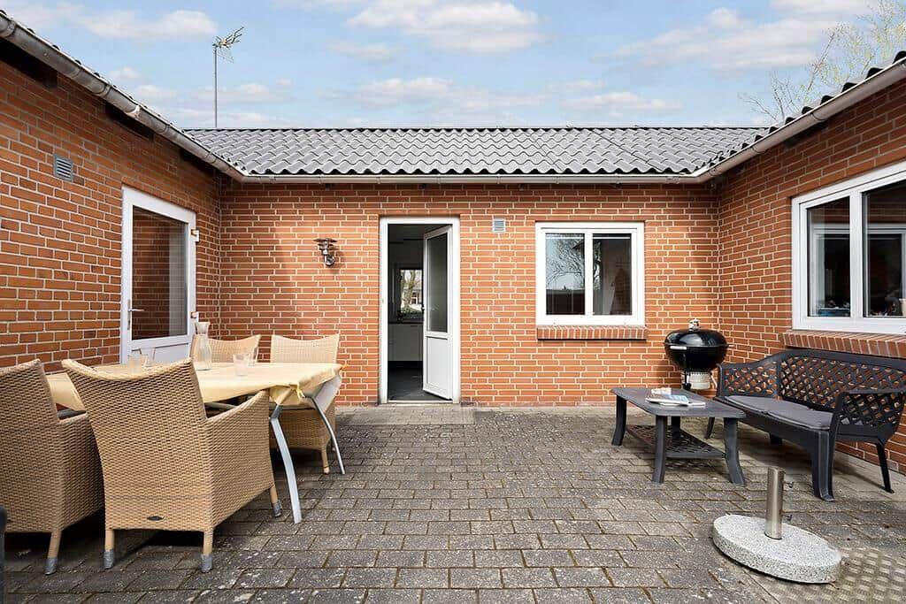 Hinterhof mit Tisch, Stühlen, Grill und Bank. Tür führt ins Haus.