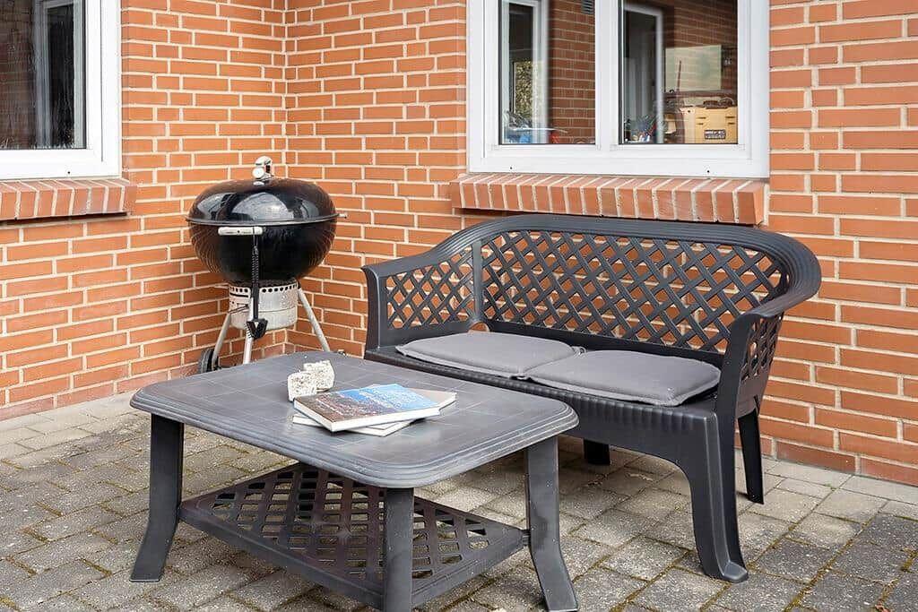 Terrasse mit Grill, Sitzbank und Tisch. Hintergrund: Backsteinmauer mit Fenstern.