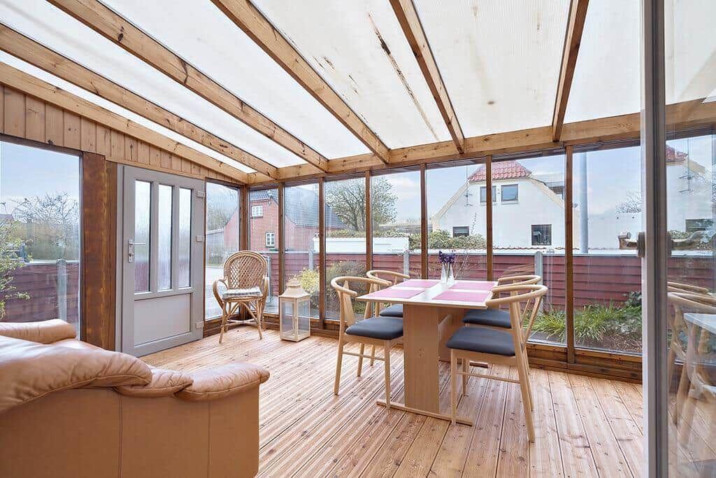 Terrasse mit Sitzgruppe, Tisch und Stühlen, Holzboden und Glaswände.