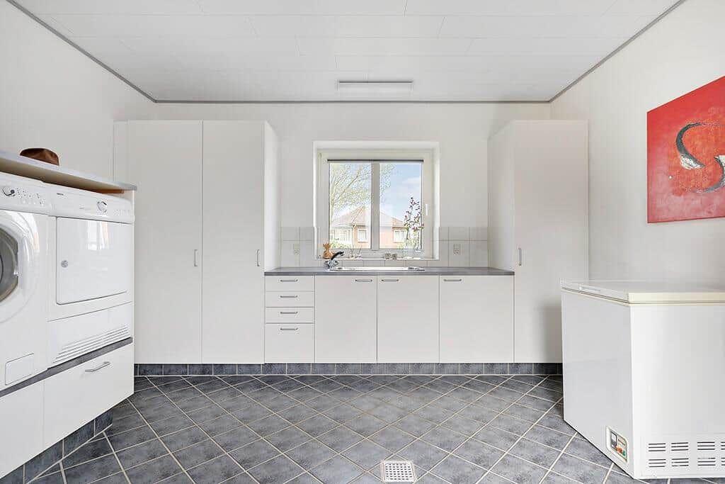 Küche mit Waschmaschine, Spüle und Kühlschrank. Fenster mit Blick nach außen.
