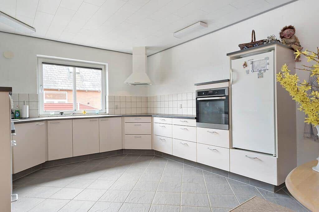 Küche mit weißen Schränken, Kühlschrank und Backofen. Fenster mit Blick auf Dach.
