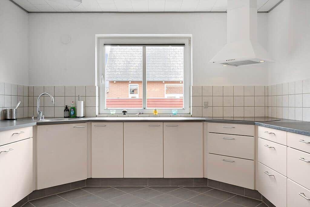 Küche mit hellen Schränken, Fenster und Dunstabzugshaube.
