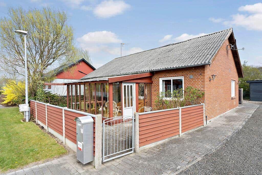 Ein Haus mit rotem Zaun und Terrasse. Vor dem Haus steht ein Briefkasten.