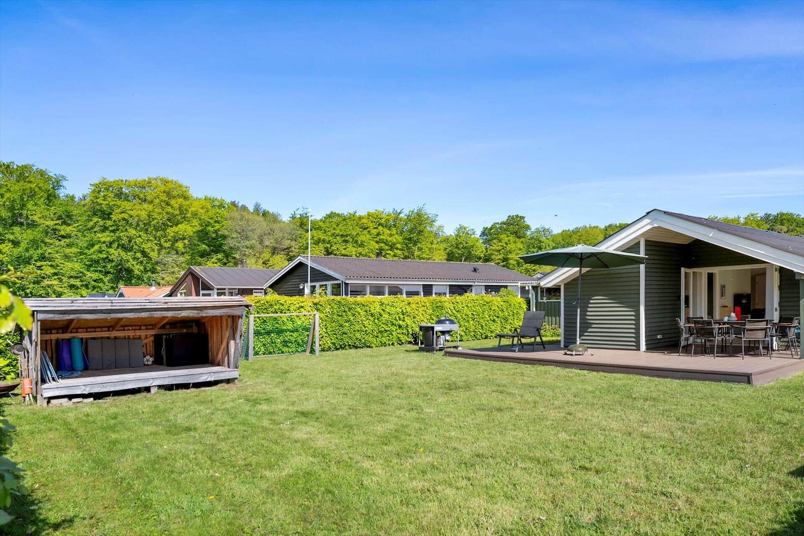 House with terrace, grill, and garden. Trees and another house are visible in the background.