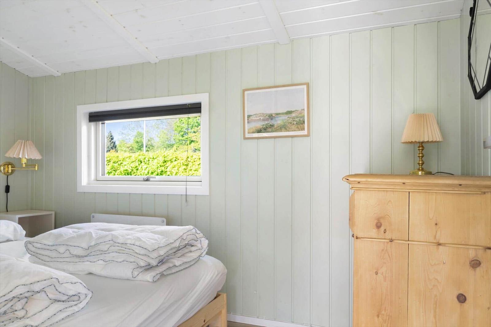 Bedroom with bed, wardrobe, and window overlooking greenery.