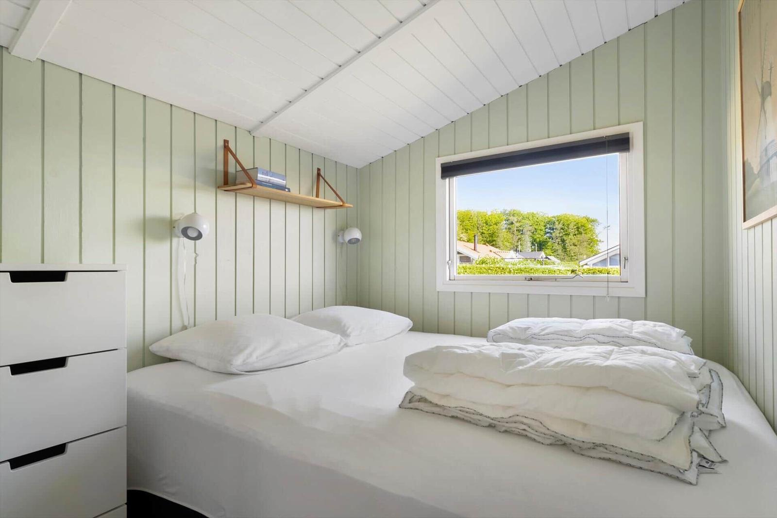 Bedroom with bed, nightstand, and window view of green areas.