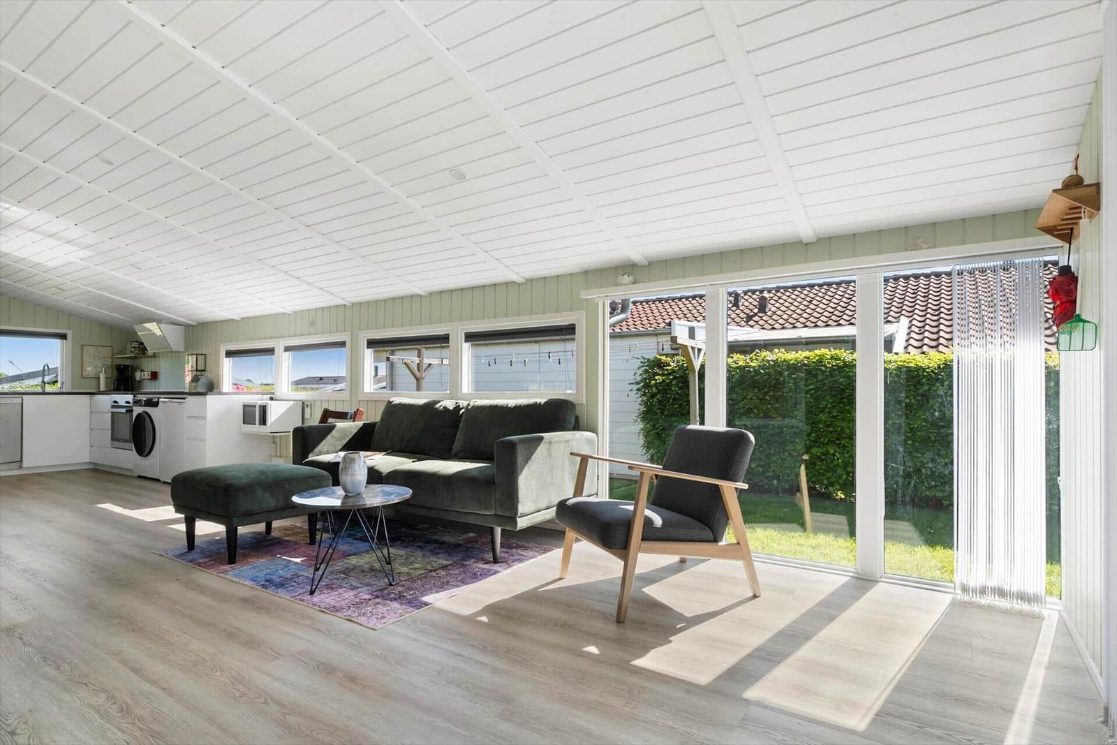 Living and kitchen area with sofa, armchair, and large window to outdoor terrace.