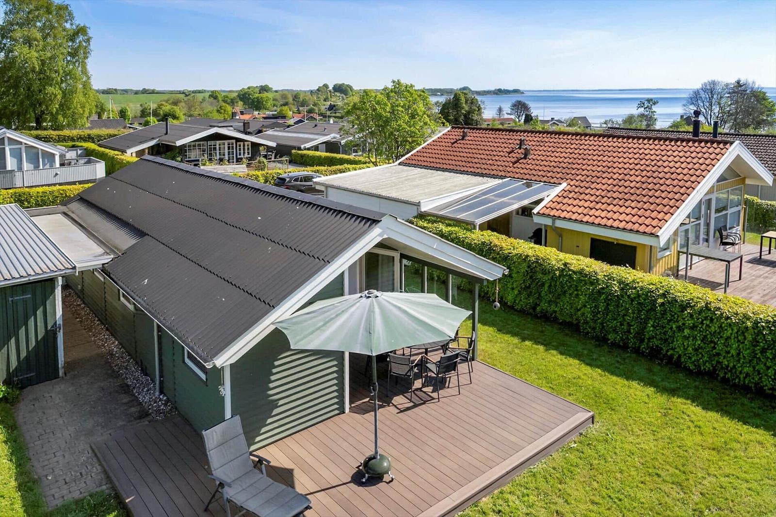 Green wooden structure with terrace, umbrella, and view of the water.