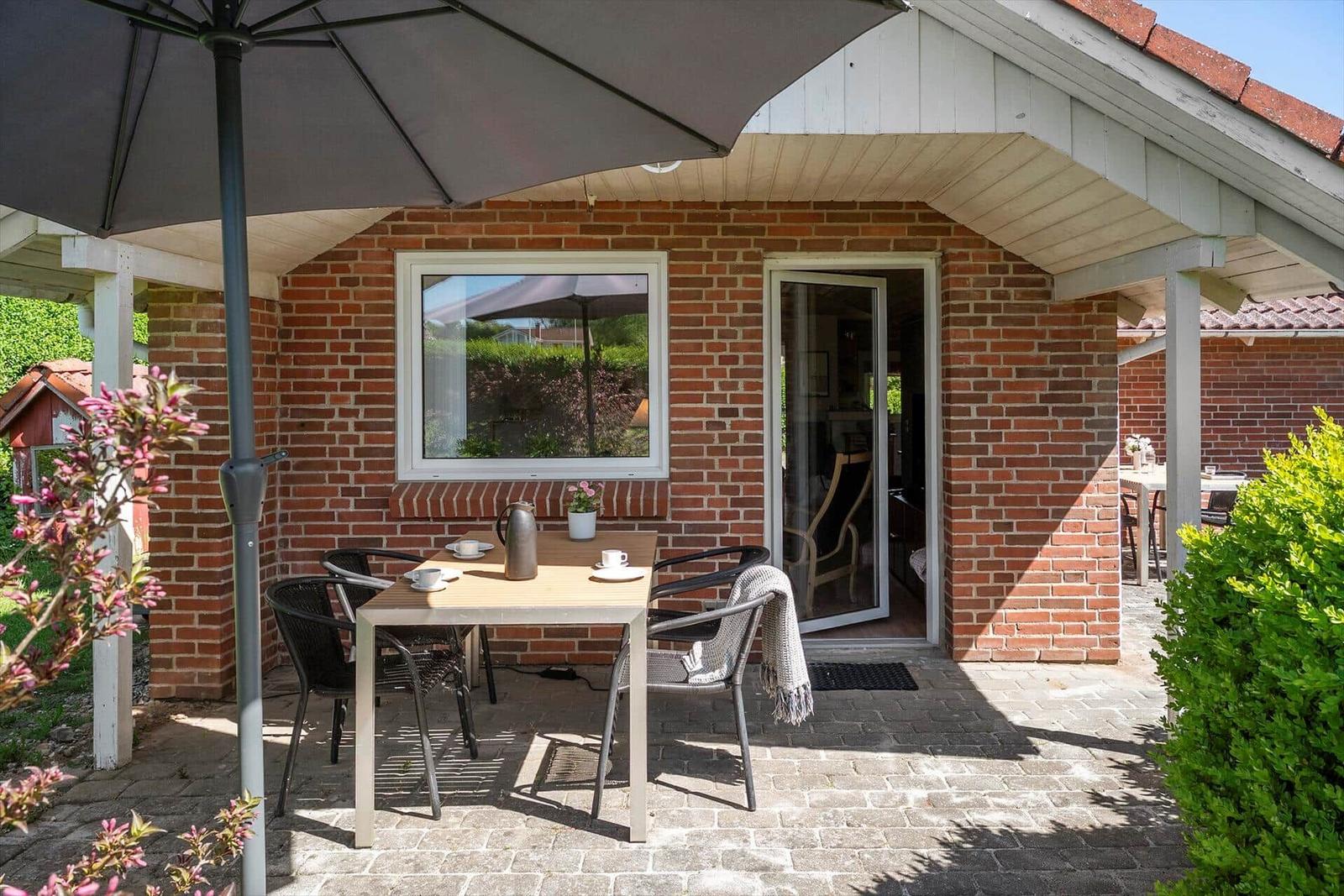 Terrace with table, chairs, and umbrella. Entrance to apartment. Garden area.