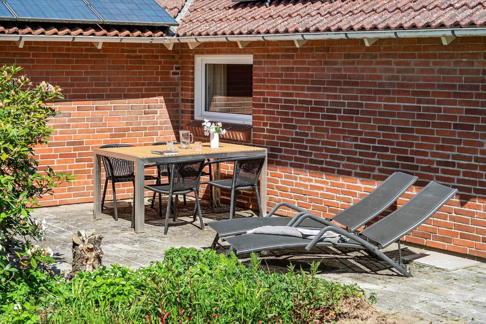 Outdoor area with table, chairs, and lounge chairs against brick wall.