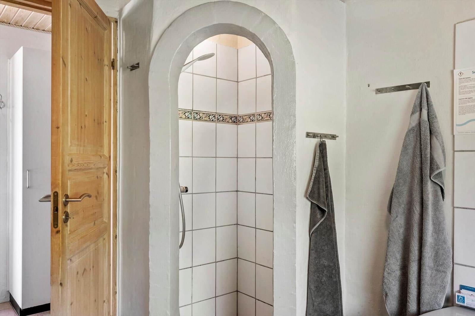 Bathroom with shower and wooden door. Towels hang on hooks.