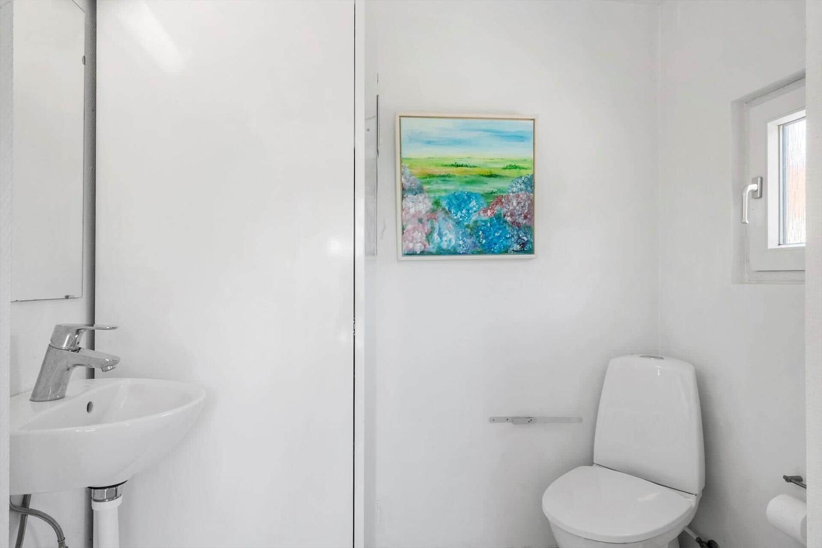 Bathroom with sink, toilet, and window. Wall art with landscape motif.