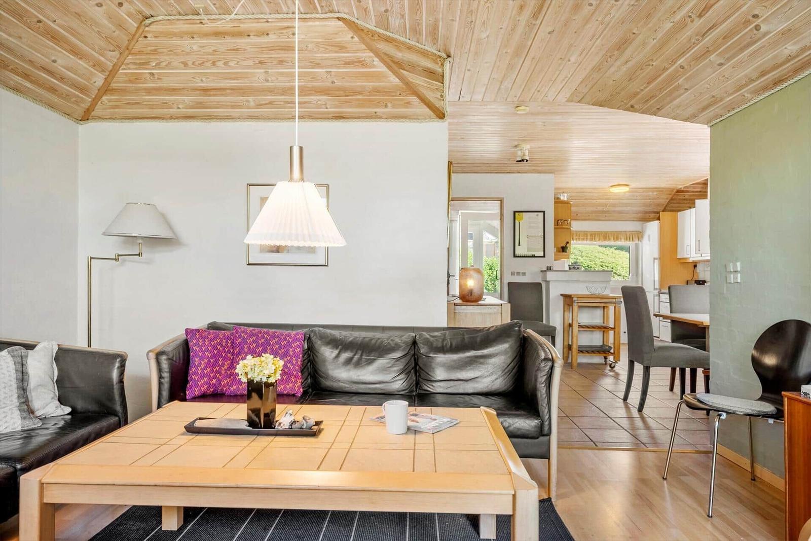 Living area with leather sofa, wooden table, and kitchen area in background.