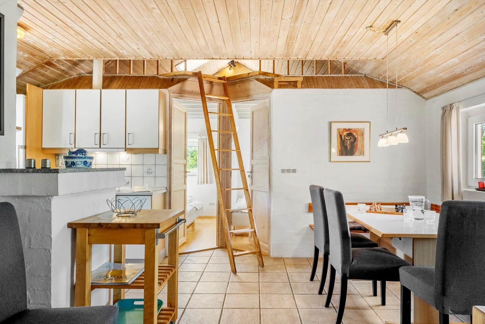 Kitchen with dining area, ladder to sleeping space, wooden ceiling, and window.