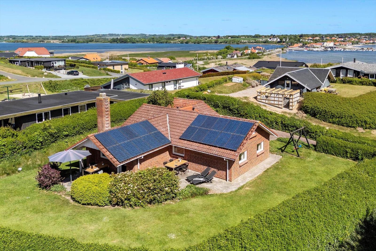 Red roof with solar panels, garden with loungers and view of water.