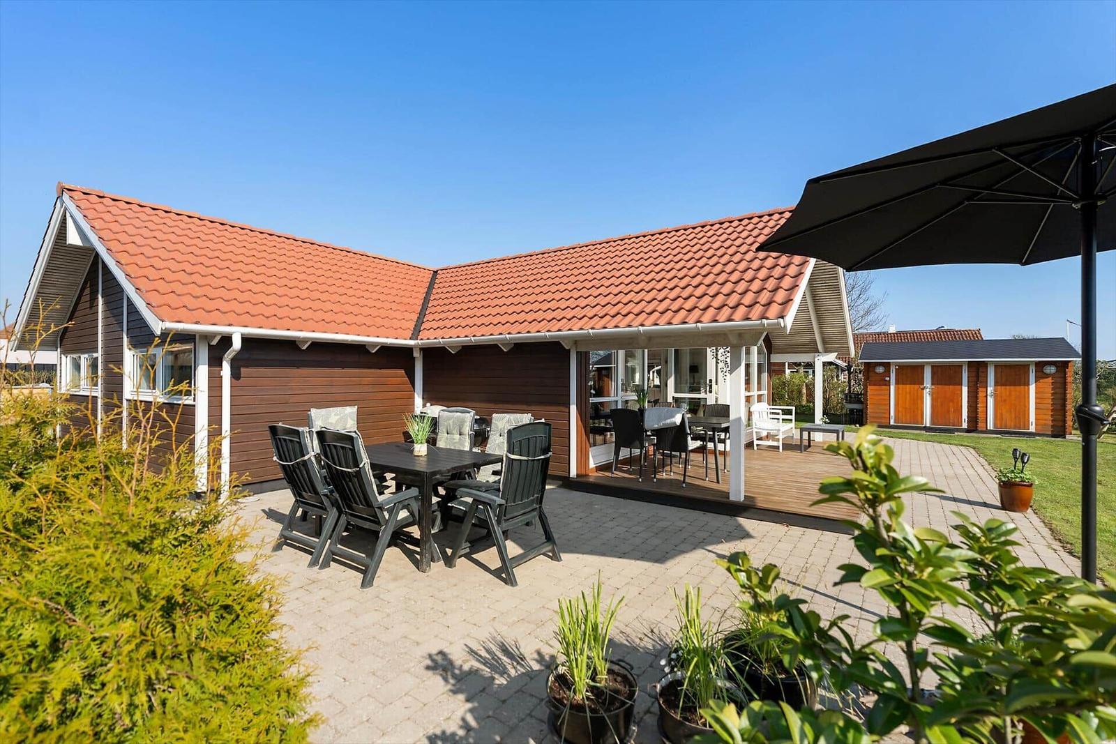 House with terrace, garden, and sunshade. Table and chairs for outdoor seating.
