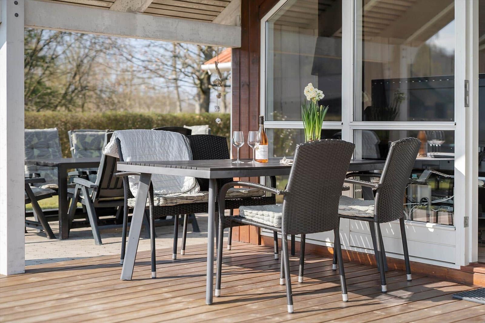 Deck with table and chairs, wine and flowers before glass facade