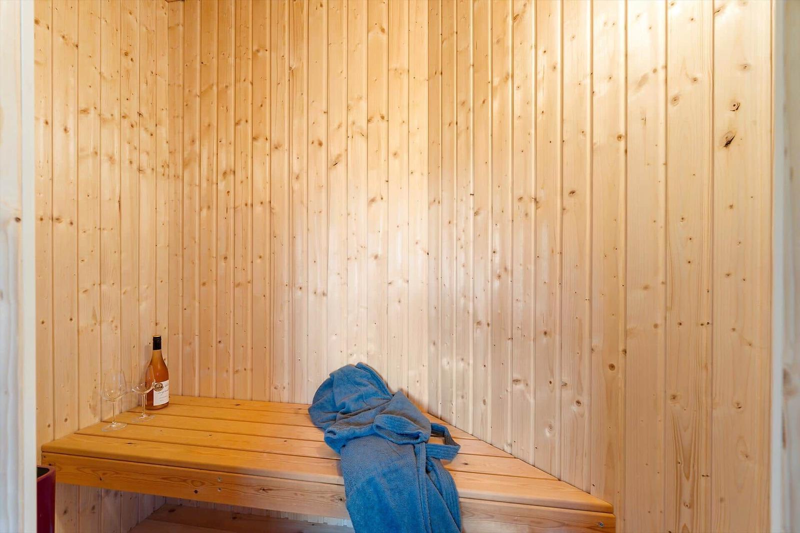 Sauna with wooden walls, bench, blue towel, and wine bottle.