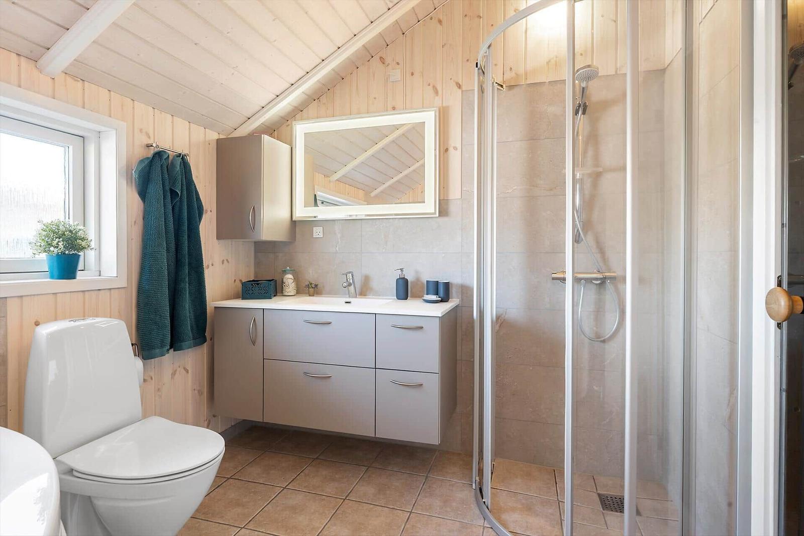 Bathroom with shower, sink and toilet. Wooden walls and window.