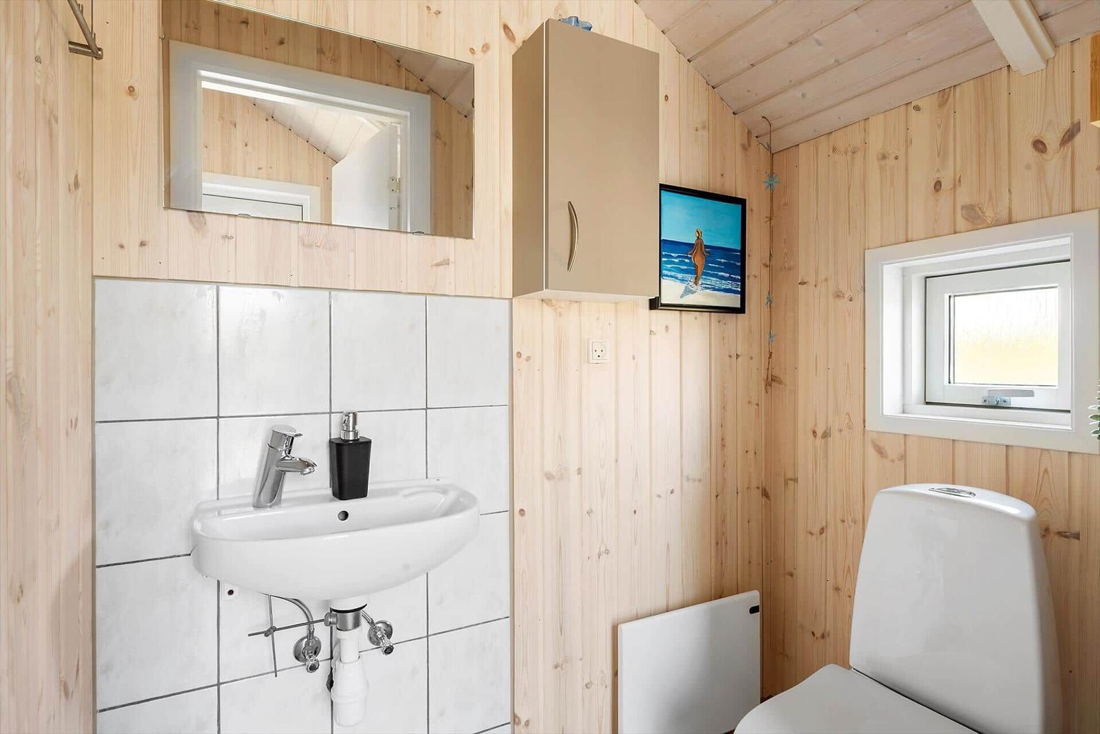 Bathroom with sink, mirror, toilet, and window.