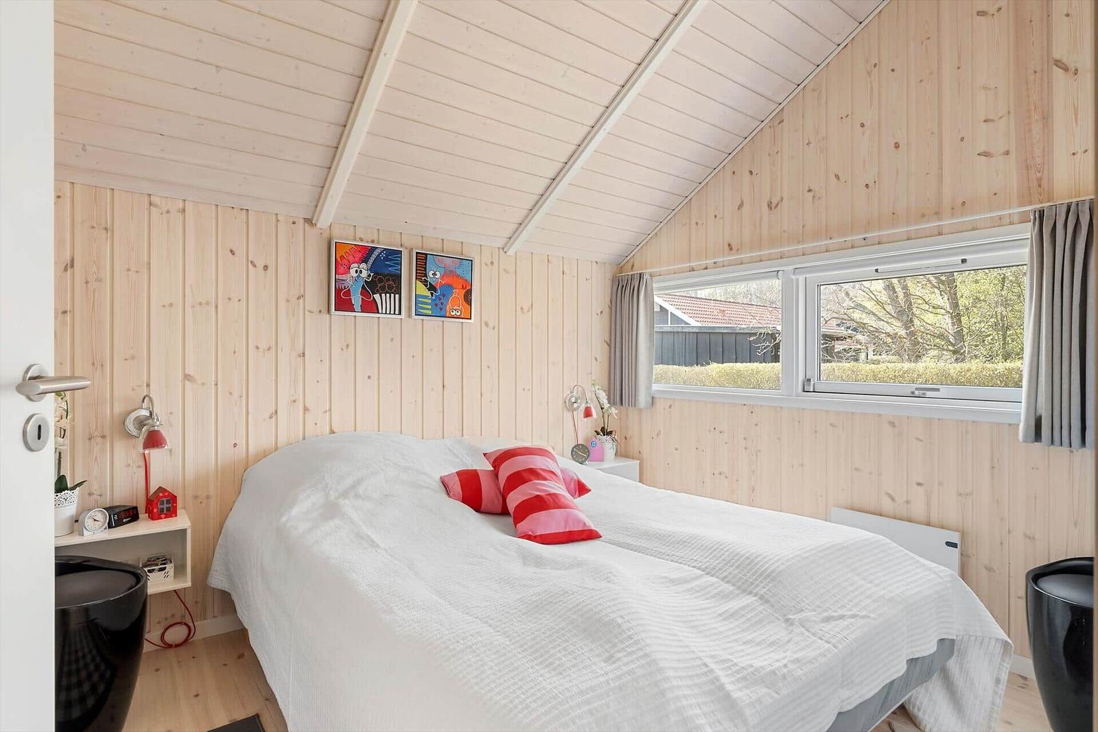 Bedroom with wooden walls, bed, window, and pictures on the wall.