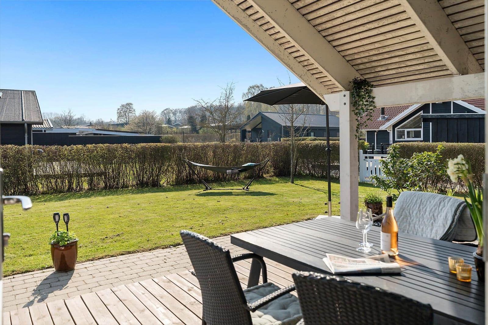 Terrace with table, chairs, and awning. In the background, a garden with hammock and hedge.