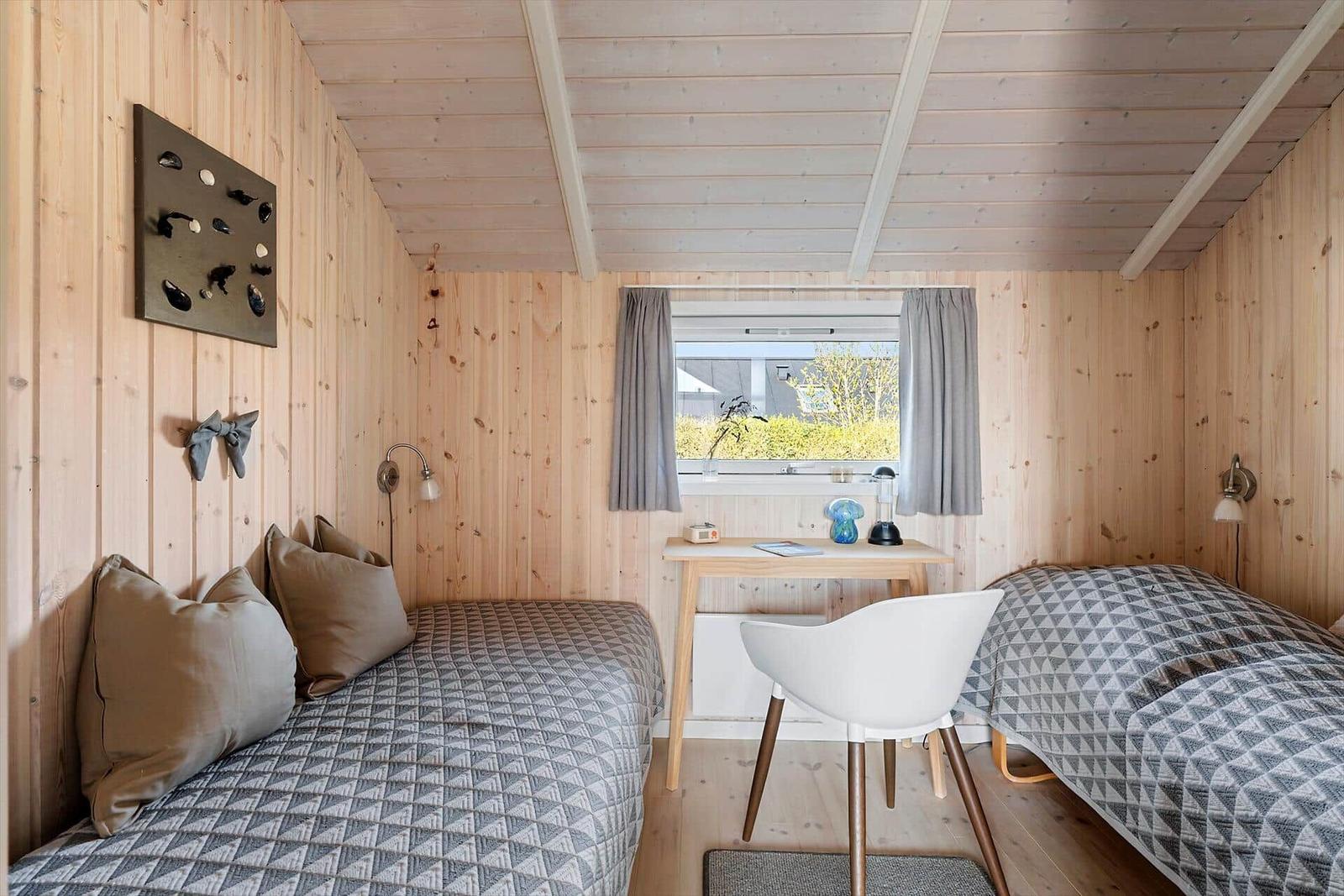 Two beds with patterned bedspreads, desk, and window with curtains.