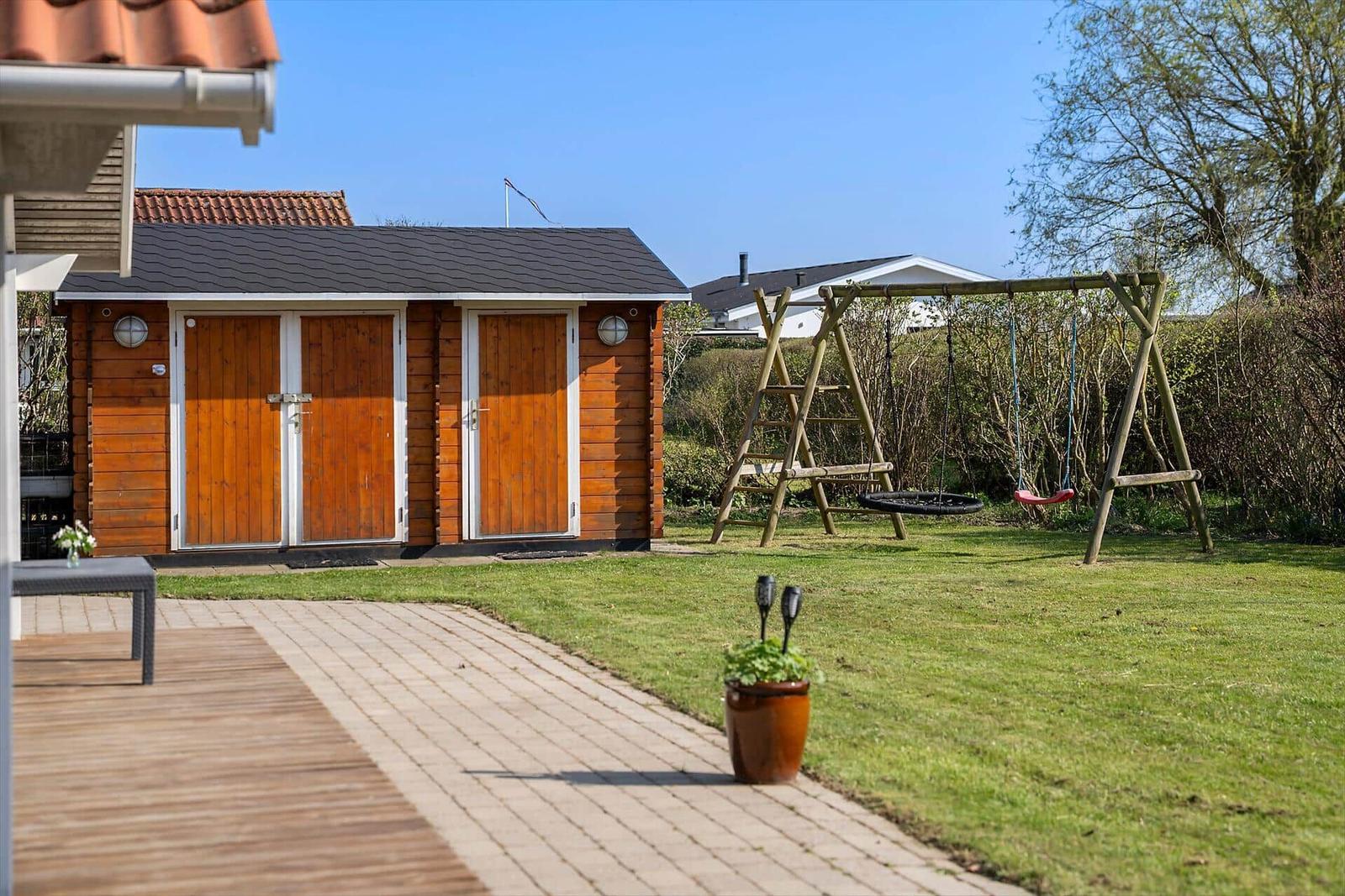 Backyard with wooden shed and play equipment on green lawn.