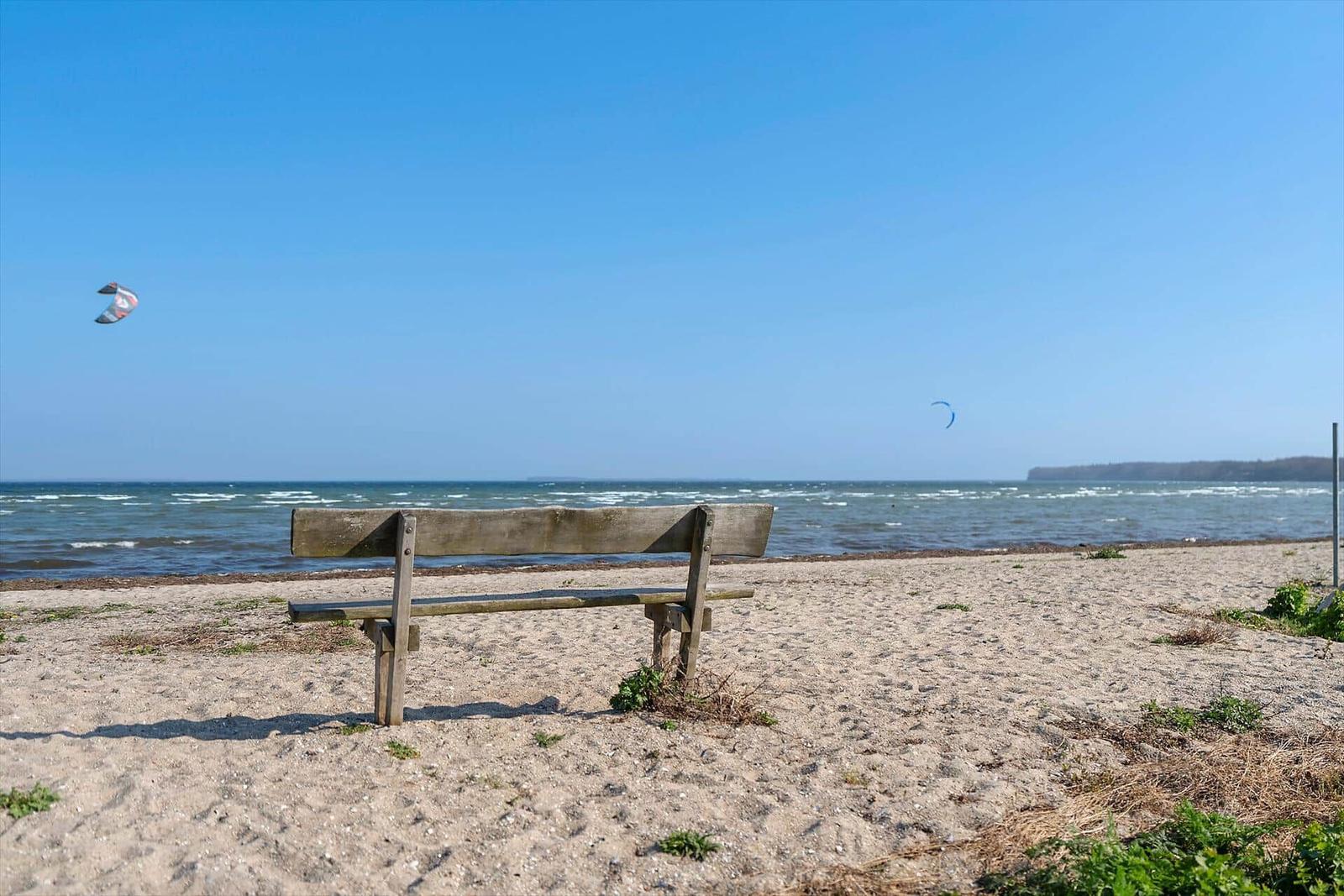 Wooden bench at the beach with kitesurfers in the background.