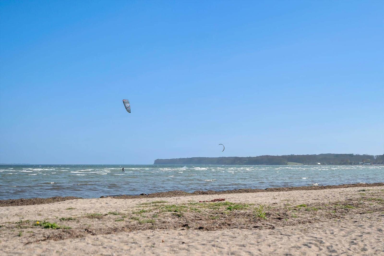 Beach with kitesurfers and clear sky.