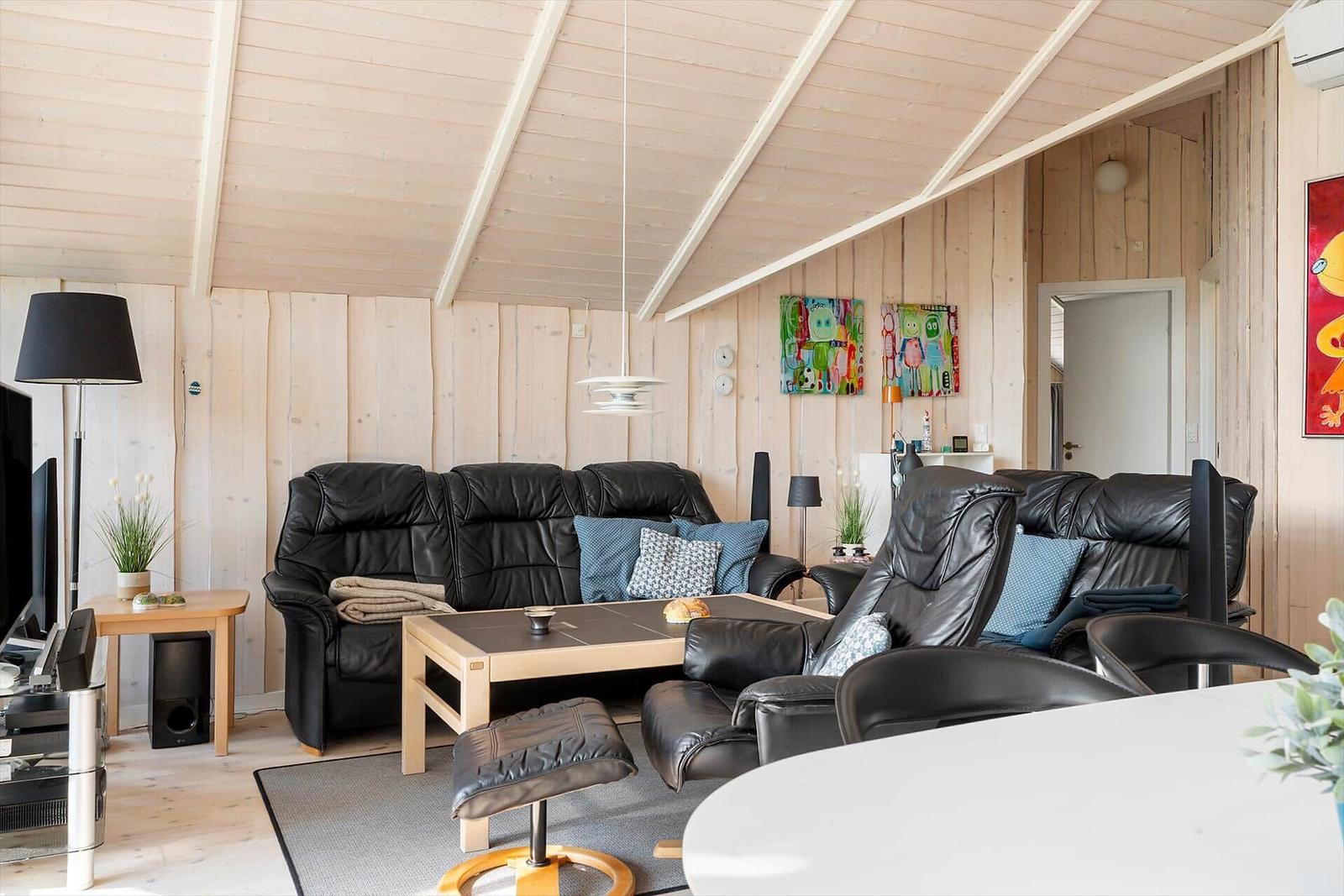Living room with black leather sofas, wooden walls and ceiling, table and wall art.